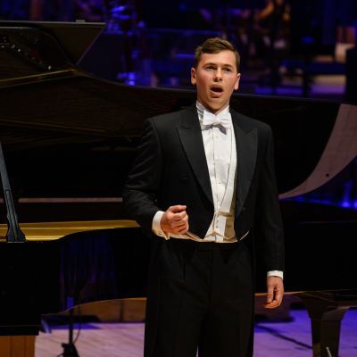 Male presenting student wearing a suit on stage singing with a piano in the background